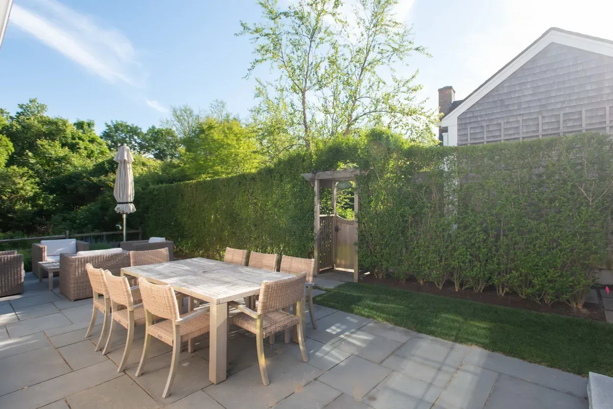 Outdoor dining table on the bluestone patio beside the hedge and arbour